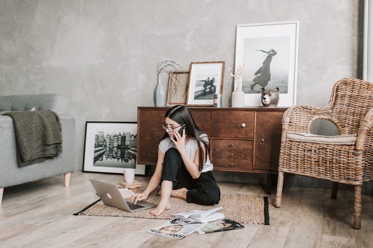 Focused young woman with laptop and smartphone in modern apartment